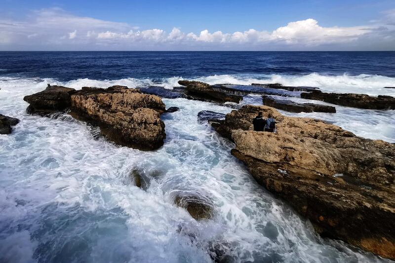 A couple sits in a rocky area as waves crash along the coastline in Beirut, Lebanon. AP Photo