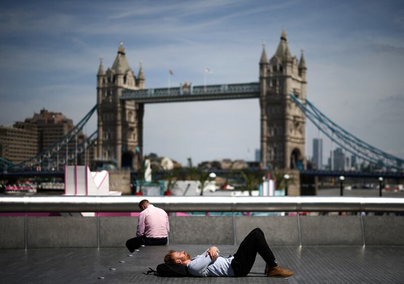 People relax in the sun on the bank of the River Thames, with the City of London financial district in the distance. Reuters