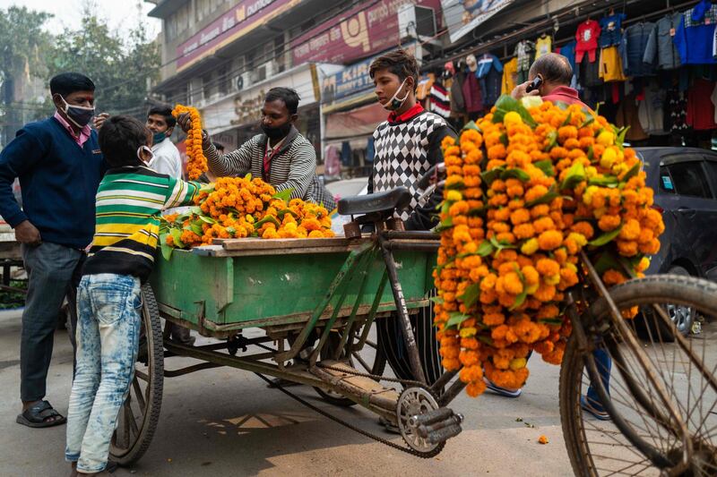 A vendor (C) selling marigold flowers for Diwali, the Hindu Festival of Lights, attends customers in a market area in New Delhi on November 14, 2020. / AFP / Jewel SAMAD
