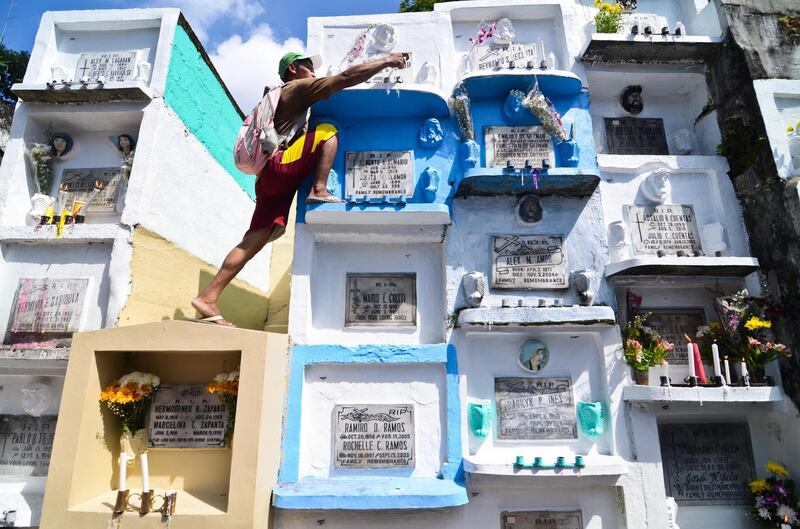 MARIKINA CITY, PHILIPPINES  A man places candles on the crypt of a loved one at a public cemetery as All Saint's Day is celebrated on November 1, 2013 in Marikina City, Philippines. As the largest Catholic nation in Asia this public holiday allows Filipinos to visit the family cemeteries for overnight and weekend vigils. They bring candles and flowers and pay respects to departed loved ones. Offices and schools close as the usually silent graveyards become a party with food and music.  (Photo by Dondi Tawatao/Getty Images)