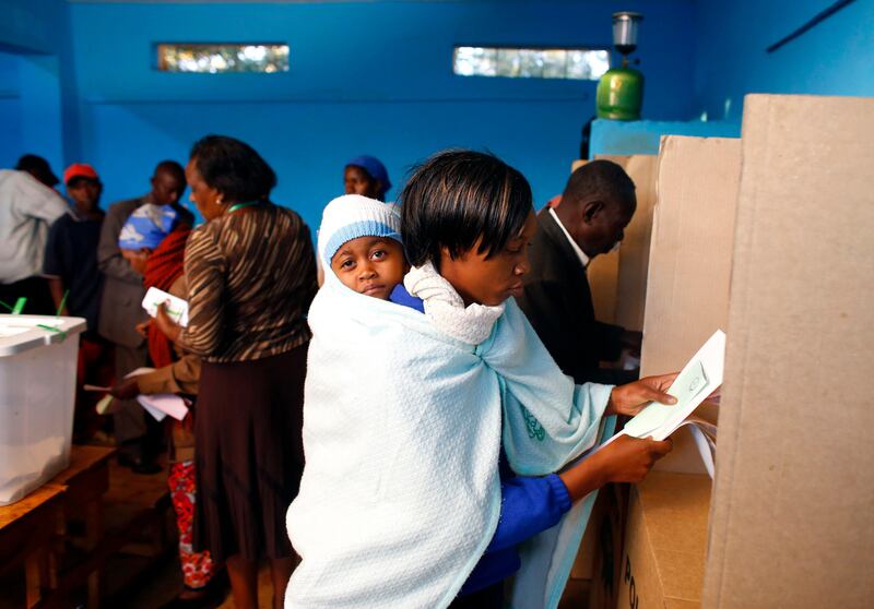 A woman with a child casts her ballot inside a polling station in Kenya's town of Gatundu March 4, 2013. Polling stations opened up to Kenyans on Monday for a tense presidential election that will test whether the east African nation can repair its damaged reputation after the tribal blood-letting that followed a 2007 poll.  REUTERS/Marko Djurica (KENYA - Tags: POLITICS ELECTIONS)