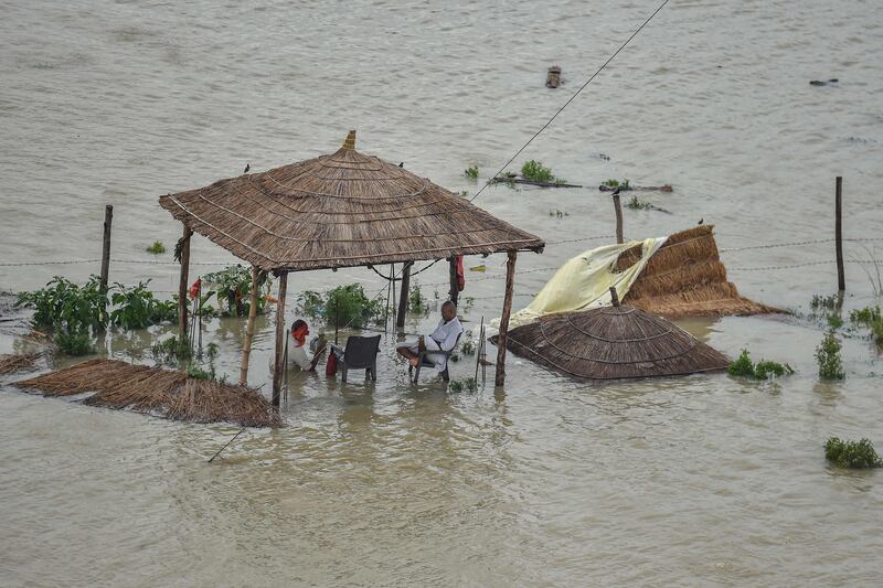 People sit under a submerged straw hut after the Ganges river banks burst in Allahabad, India.
