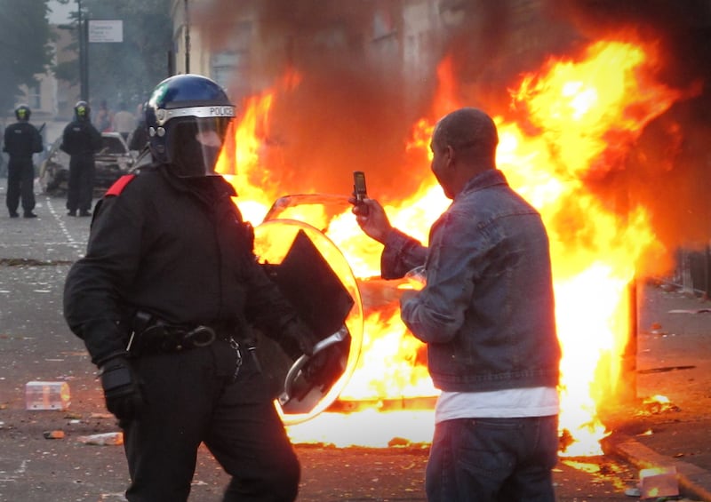 A resident films a police officer on his mobile phone during disturbances in Hackney.