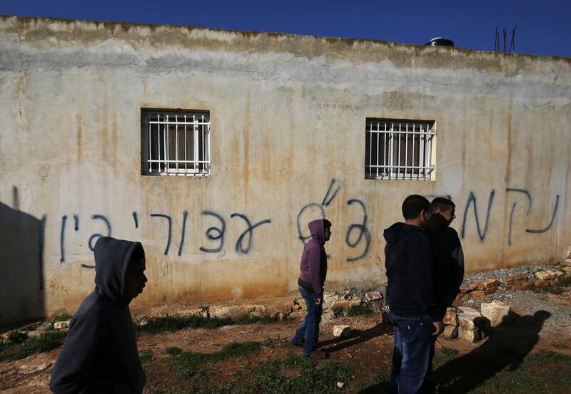 Palestinians gather next to a house sprayed with graffiti reading in Hebrew: "revenge" and "hello from the prisoners of Zion", in the village of Beitillu, near Ramallah in the Israeli occupied West Bank on December 22, 2015. Abbas Momani / AFP Photo

