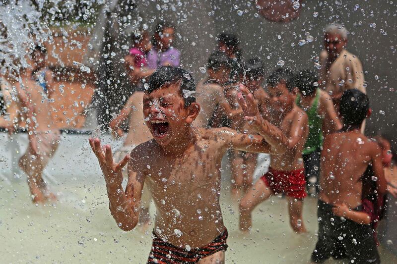 A Syrian boy reacts as he gets sprayed with water in a portable swimming pool set up by volunteers, at a camp for the displaced in the rebel-held town of Kafr Yahmul in the northern countryside of Idlib on August 10, 2022.  (Photo by aaref watad  /  AFP)