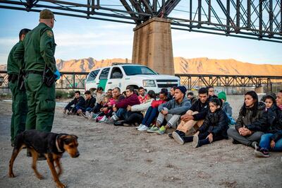 TOPSHOT - A group of about 30 Brazilian migrants, who had just crossed the border, sit on the ground near US Border Patrol agents, on the property of Jeff Allen, who used to run a brick factory near Mt. Christo Rey on the US-Mexico border in Sunland Park, New Mexico on March 20, 2019.  The militia members say they will patrol the US-Mexico border near Mt. Christo Rey, "Until the wall is built." In recent months, thousands of Central Americans have arrived in Mexico in several caravans in the hope of finding a better life in the United States. US President Donald Trump has branded such migrants a threat to national security, demanding billions of dollars from Congress to build a wall on the southern US border. / AFP / Paul Ratje
