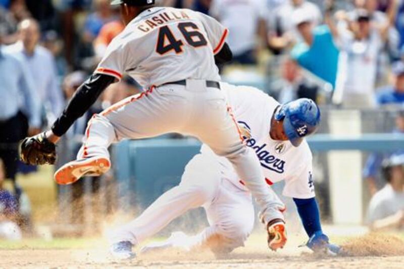 Los Angeles Dodgers' Carl Crawford slides for home as San Francisco Giants' pitcher Santiago Casilla leaps in the air.