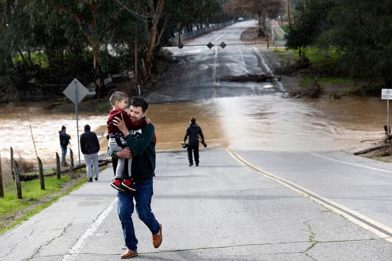 Marcial Calleja Aguirre runs with son Oliver as it starts to rain at the Silvas crossing at Uvas Creek in Gilroy. EPA  