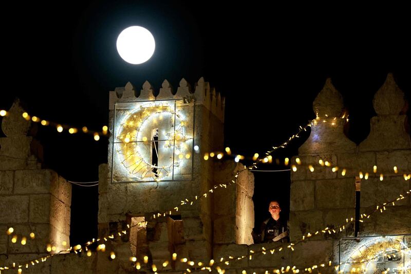 TOPSHOT - April's full moon, known as the Super Pink Moon, rises over the Damascus gate as an Israeli police stands guard in Jerusalem's Old City on April 27, 2021. / AFP / Menahem KAHANA
