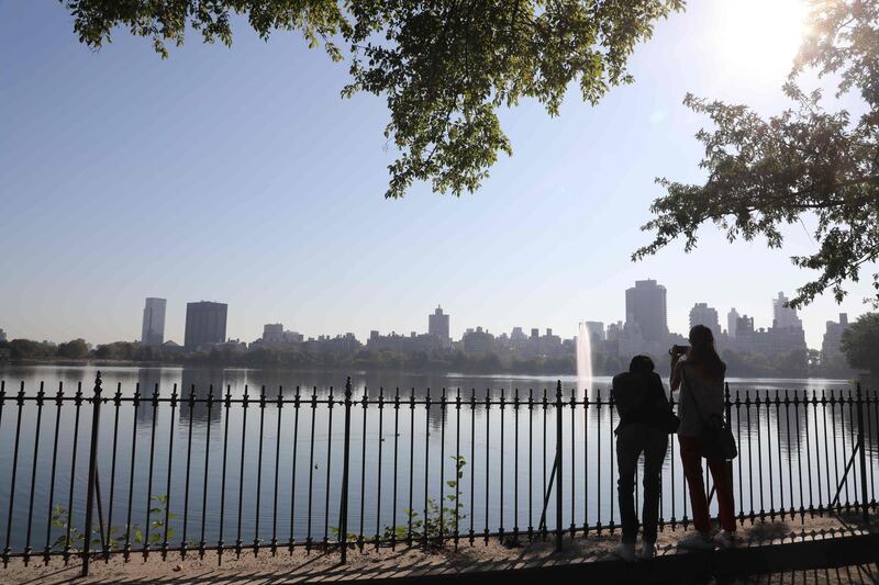 People take a break under a tree as they look at the Manhattan skyline from around the Jacqueline Kennedy Onassis reservoir in Central Park in New York.  AFP