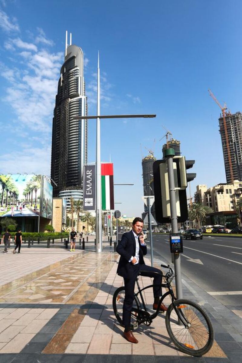 A businessman waits to cross Sheikh Mohammed bin Rashid Boulevard with The Address Hotel in the background.