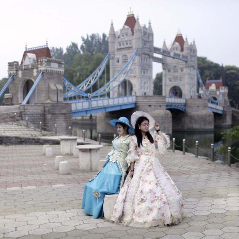 Two Chinese girls wearing costumes posing for a photo before a mini replica of the London tower bridge.