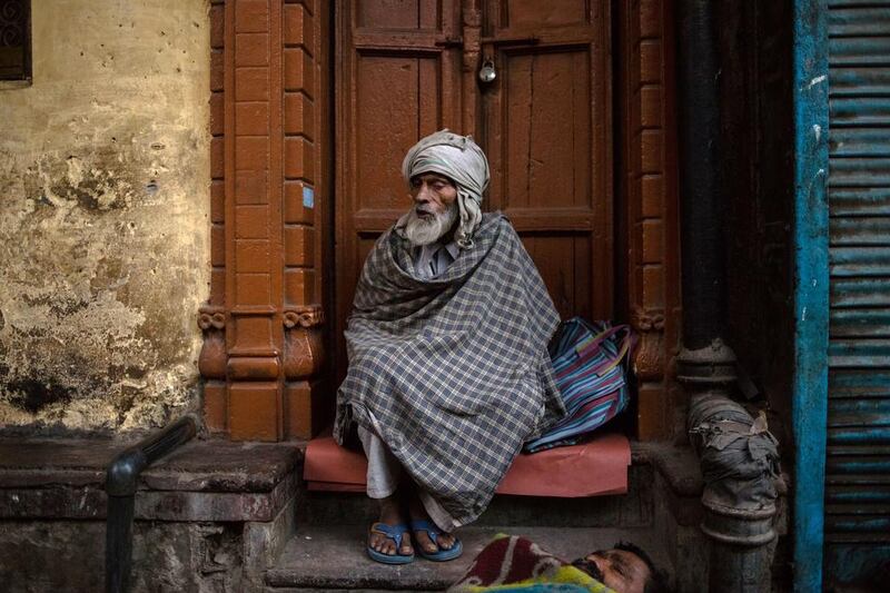 Indian resident Mohammad Razar, who says he is aged around 60, sits in a doorway as a fellow resident sleeps in New Delhi. Rebecca Conway / AFP