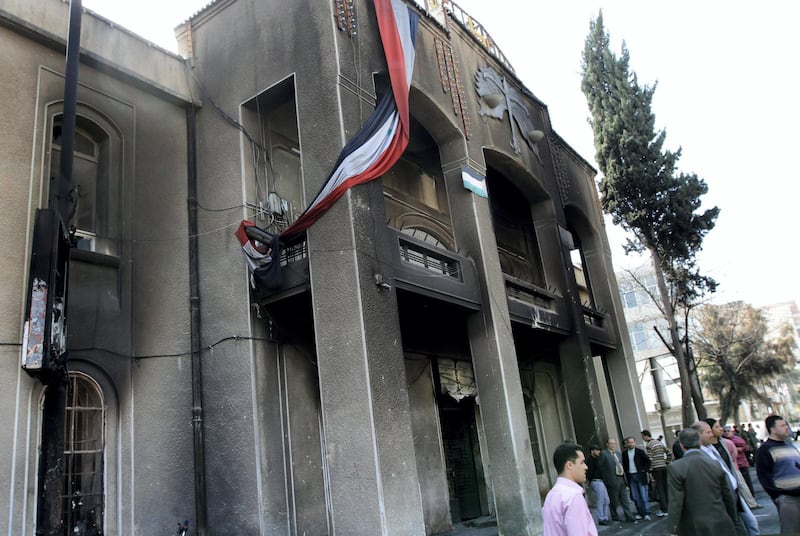 (FILES) In this file photo taken on March 21, 2011, Syrian men gather outside the courthouse that was torched a day earlier by angry protesters in the southern town of Daraa, 100 kms (60 miles) south of Damascus. - As it enters its tenth year, the war in Syria is anything but abating as foreign powers scrap over a ravaged country where human suffering keeps reaching new levels. (Photo by Louai Beshara / AFP)