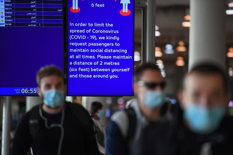 An information board displays an alert for passengers to maintain distance from others at Dubai International Airport.