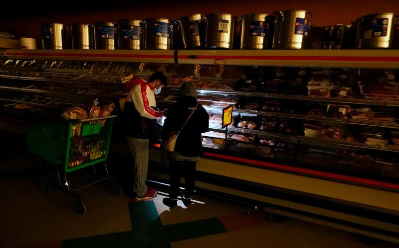 Customers use the light from a mobile phone to look in the meat section of a grocery store in Dallas. Though the store lost power, it remained open for cash-only sales. AP