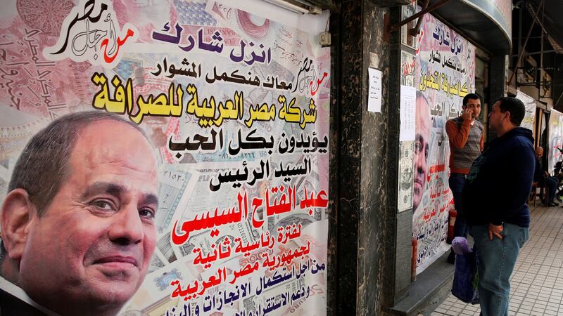 People are seen in front of an exchange bureau, with an advertisement showing images of the U.S. dollar and other foreign currency and a poster supporting Egypt's President Abdel Fattah al-Sisi for the upcoming presidential election in Cairo, Egypt March 14, 2018. Picture taken March 14, 2018. REUTERS/Amr Abdallah Dalsh?