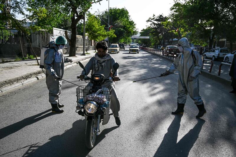 Volunteers wearing protective gear spray disinfectant on a motorist riding a motorbike, in Kabul.  AFP