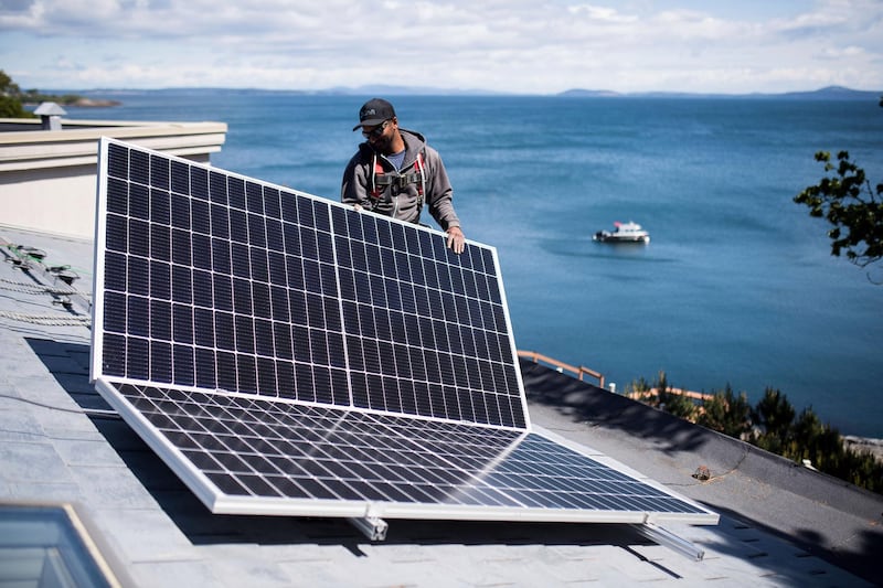 A worker places a solar panel into position on a roof during a Shift Energy Group solar installation on a home in Victoria, British Columbia, Canada, on Tuesday, May 18, 2021. Last December, the Trudeau government outlined the steps Canada would need to take to reach net-zero carbon emissions by 2050, including government grants for homeowners for energy retrofits and a need for rooftop solar installers, CBC News reported. Photographer: James MacDonald/Bloomberg