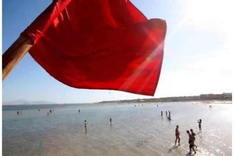 A red flag serving as a warning of shark sightings flutters over tourists enjoying a day on the beach at the Red Sea resort of Sharm el-Sheikh, Egypt.