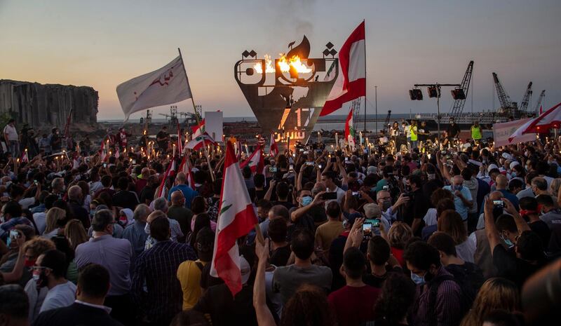 Lebanese anti-government protesters carry placards and hold a torch as they gather in front of a statue, representing the torch of the revolution, to mark the first anniversary of the anti-government protests, near the Beirut port.  EPA