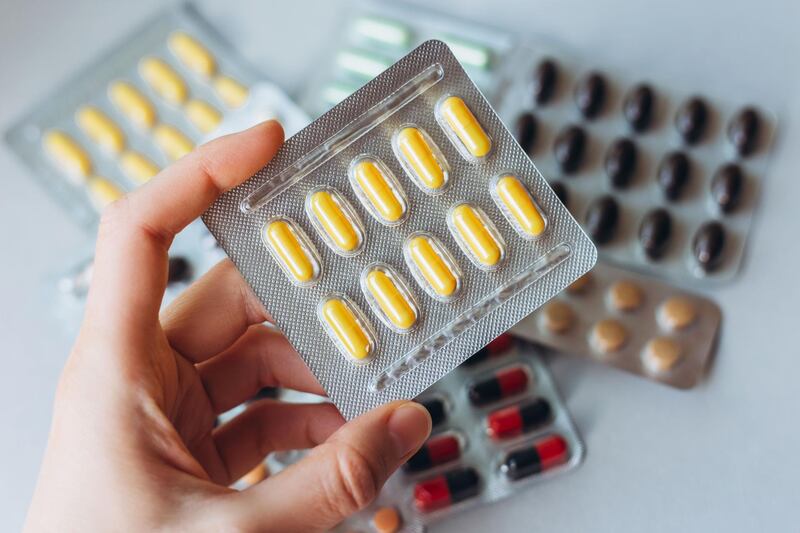 A female hand holds a package of yellow pills on the background of a heap of colored pills in packages. Getty Images