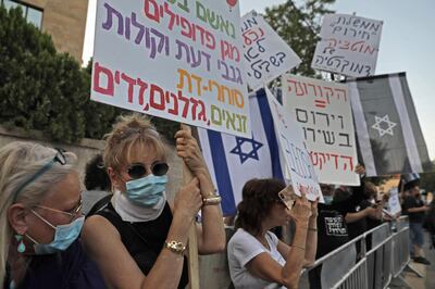 Israeli demonstrators, wearing protective masks amid the COVID-19 pandemic, carry placards during a demonstration against Prime Minister Benjamin Netanyahu in front of his residence in Jerusalem, on May 17 2020, as Israel's parliament swore in a new unity government. After more than 500 days without a stable government and three inconclusive elections, lawmakers in the 120-seat parliament approved a three-year coalition, with 73 voting for and 46 against. One member was absent. The new government was set to confront serious crises in its first weeks, including the economic devastation wrought by the coronavirus and a looming battle over Israel's possible annexation of large parts of the occupied West Bank. / AFP / MENAHEM KAHANA
