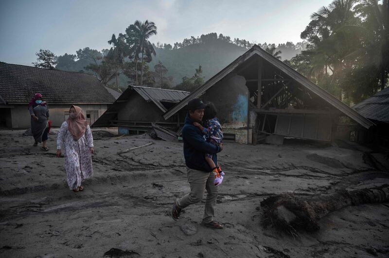 People walk past homes covered with ash and mud. AFP