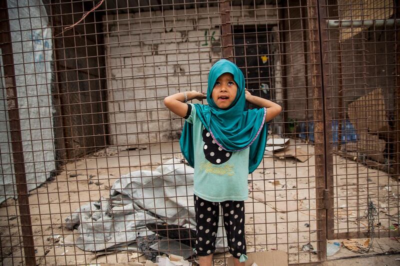 A girl poses for a photograph as she stands in front of one of the closed shops at al-Hol camp that houses some 60,000 refugees, including families and supporters of the Islamic State group, many of them foreign nationals, in Hasakeh province, Syria, Saturday, May 1, 2021. Kurdish officials say security has improved at the sprawling camp in northeast Syria, but concerns are growing of a coronavirus outbreak in the facility. (AP Photo/Baderkhan Ahmad)