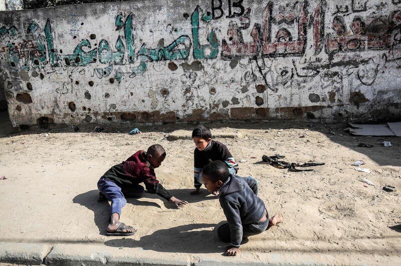 Palestinian children trace lines in sand on the pavement at the Rafah refugee camp in the southern Gaza strip on February 4, 2018. / AFP PHOTO / SAID KHATIB