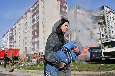 CORRECTION / TOPSHOT - A woman walks past damaged residential buildings as she carries a child in Uman, around 215km southern Kyiv, on April 28, 2023, after Russian missile strikes targeted several Ukrainian cities overnight.   Ukraine and Russia have been fighting since Moscow's February 2022 invasion and Ukraine says it has been preparing for months a counter-offensive aimed at repelling Russian forces from the territory they currently hold in the east and south.
 (Photo by Sergei SUPINSKY / AFP)
