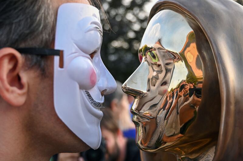 A man wearing a Guy Fawkes mask with the Nakamoto sculpture