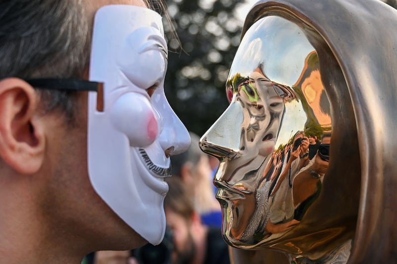 A man wearing a Guy Fawkes mask with the Nakamoto sculpture