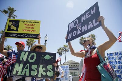 FILE - Demonstrators hold signs as they protest the lockdown and wearing masks Saturday, June 27, 2020, in Huntington Beach, Calif. After weeks of stressing education over enforcement, California communities say they are now issuing fines and relying on anonymous tips to make sure businesses and residents are complying with health orders requiring masks, disinfection, and social distancing as the state tries to contain the coronavirus.(AP Photo/Marcio Jose Sanchez, File)