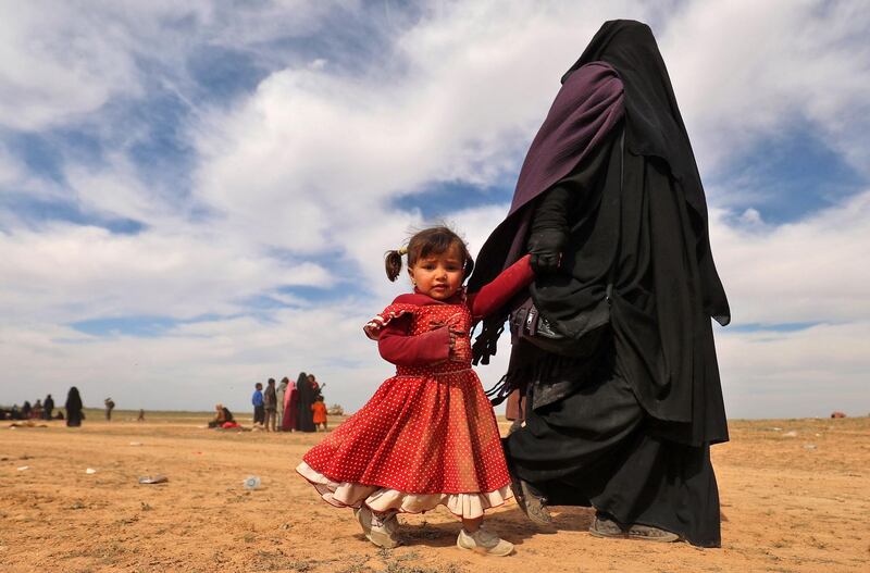 A woman walks with her daughter as civilians flee the Islamic State's group embattled holdout of Baghouz, Syria. AFP