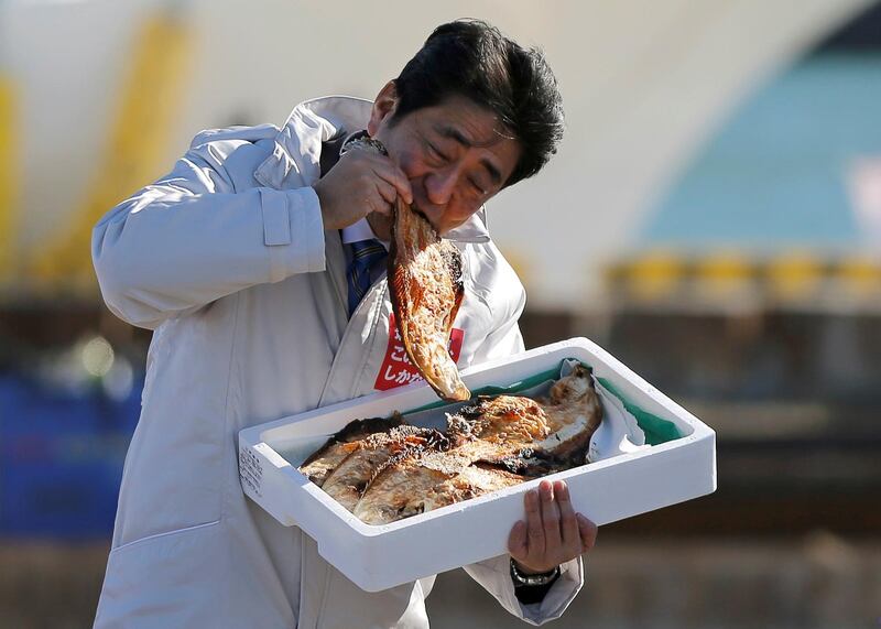 Japan's Prime Minister Shinzo Abe  eats a local grilled fish at the Soma Haragama fishing port in Soma, Fukushima prefecture, December 2, 2014. Reuters