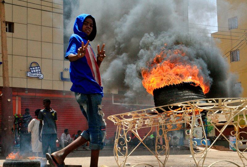 A Sudanese protester gestures as he walks past burning tyre near Khartoum's army headquarters on after security forces broke up a weeks-long sit-in. AFP