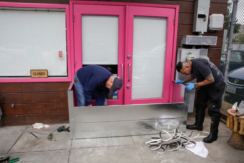 Men install a floodgate in front of Pink Onion, a pizza shop in the Mission District in San Francisco. San Francisco Chronicle / AP