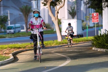 Cyclists on a pathway ride along the Corniche in Abu Dhabi wearing protective masks. Victor Besa/The National 