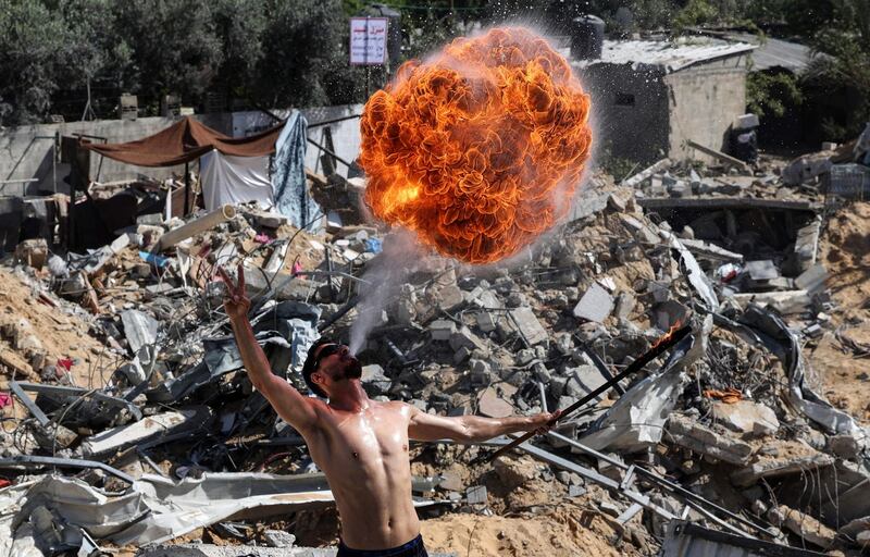 A member of Gaza's Bar Woolf sports team performs with fire above the ruins of a building destroyed in recent Israeli air strikes in Beit Lahia. AFP