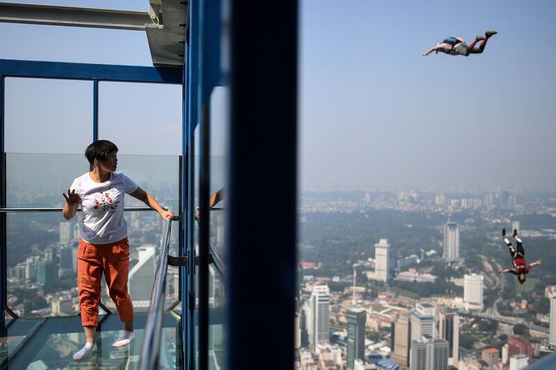 A tourist watches as base jumpers leap from the 300-metre-high skydeck of Malaysia's landmark Kuala Lumpur Tower against the backdrop of the city's skyline. AFP
