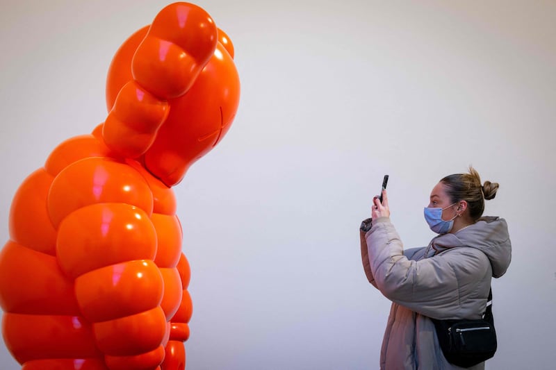 A visitor takes a photo of an artwork titled 'Kaws What Party' from the New Fiction exhibition. AFP