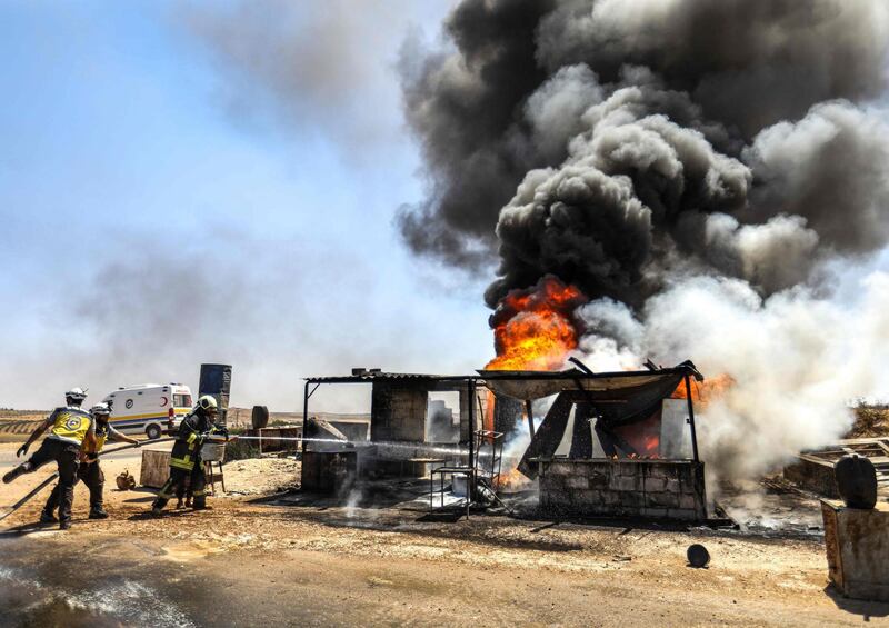 TOPSHOT - Firefighters from the Syrian Civil Defence, also known as the "White Helmets", extinguish a fire at a vehicle gathering point for fleeing civilians, which was hit by reported government forces' bombardment, in Maar Shurin on the outskirts of Maaret al-Numan in Syria's northwestern Idlib province on August 25, 2019.  / AFP / Omar HAJ KADOUR
