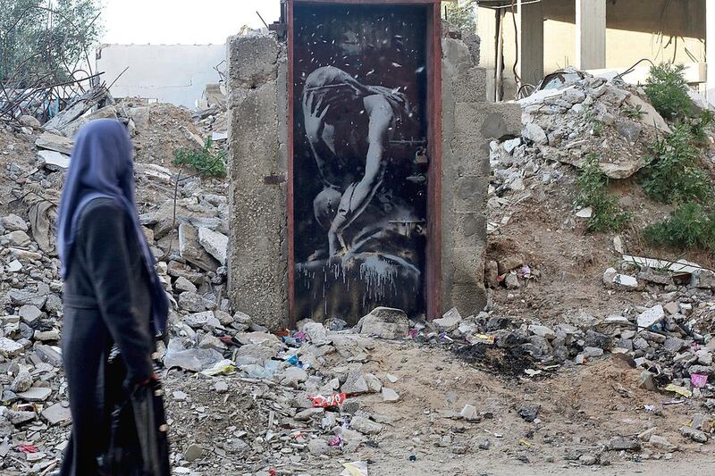 File photo of a woman walking past a mural painted by British street graffiti artist Banksy on a door of a house which was destroyed during the 2014 conflict between Israel and Hamas in the northern Gaza Strip. Mohammed Saber/EPA