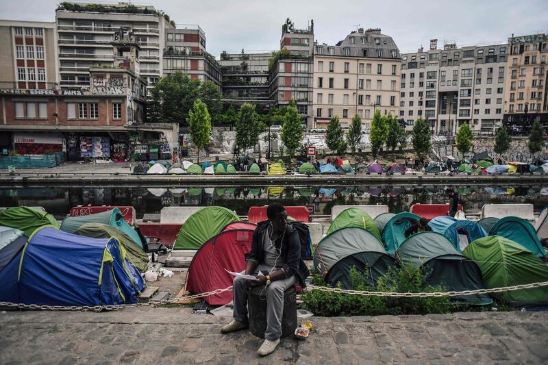 A man sits as migrants prepare their belongings at the start of the clearing by police of their makeshift camp along the Canal de Saint-Martin at Quai de Valmy in Paris. Lucas Barioulet / AFP