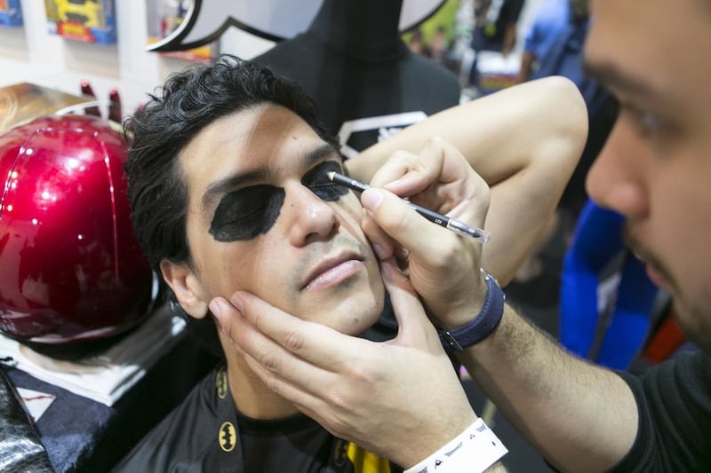 A man puts on eye make up on his friend, before he dons his Batman costume.