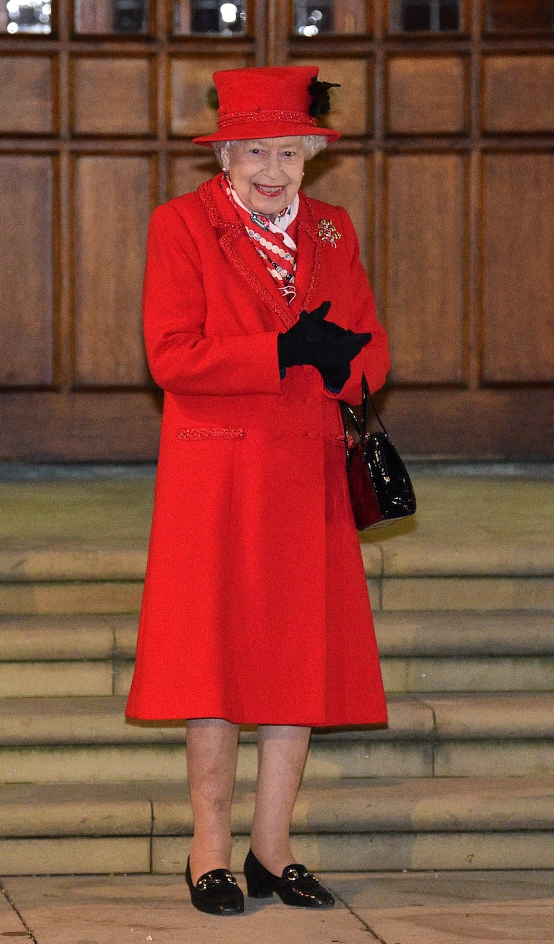 Queen Elizabeth II, wearing red, waits to thank local volunteers and key workers for their efforts amid the coronavirus pandemic, at Windsor Castle on December 8, 2020. Getty Images