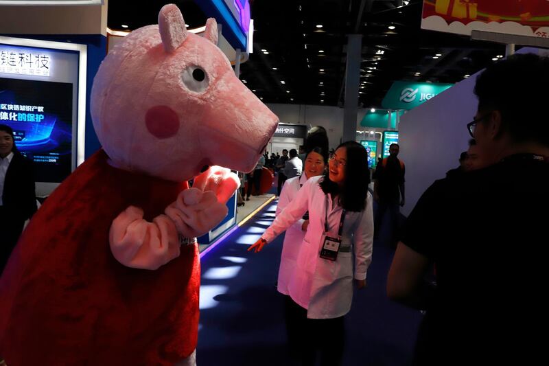 FILE  - In this April 27, 2018 file photo, a woman reacts to a Peppa Pig mascot during the Global Mobile Internet Conference (GMIC) in Beijing, China. Hasbro is going whole hog on Peppa Pig. The maker of Monopoly and GI Joe will pay about $4 billion to buy Entertainment One Ltd, a British entertainment company that produces "Peppa Pig," "PJ Masks" and other animated shows for preschoolers. (AP Photo/Ng Han Guan. File)