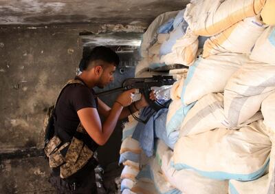 Moawiya Sayasina, the Syrian activist who started scribbling anti-Assad slogans in 2011, aims a Kalashnikov assault rifle through sandbags at a fortified position near the frontline in a rebel-held neighbourhood in the southern Syrian city of Daraa on June 5, 2018. "Your turn, Doctor." Seven years after scribbling the anti-Assad slogan that sparked Syria's war, activists-turned-rebels Moawiya and Samer Sayasina are bracing themselves for a regime assault on their hometown Daraa. / AFP / Mohamad ABAZEED
