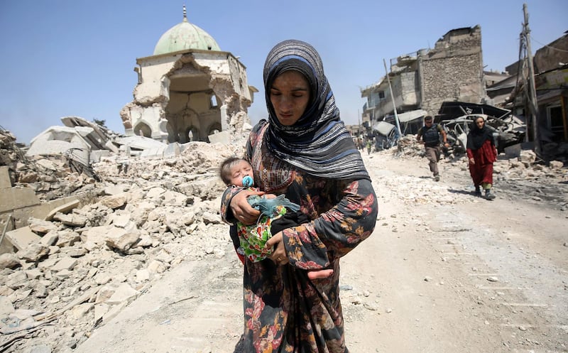 An Iraqi woman, carrying an infant, walks by the destroyed Al Nuri Mosque in July 2017. AFP